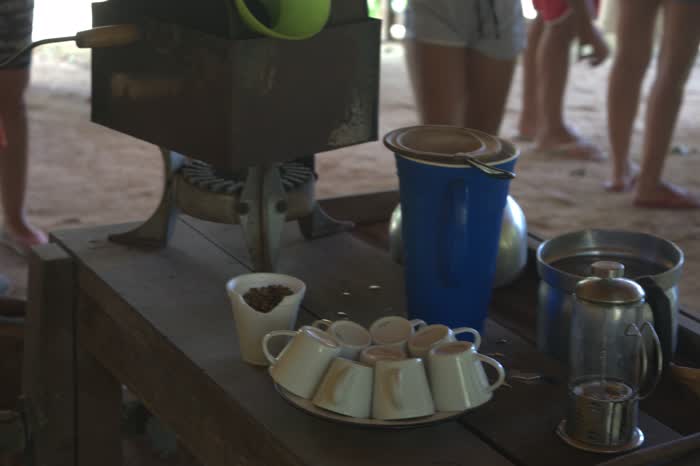 A estação do café montada sob o telheiro: o torrador de ferro sobre a bancada, xícaras brancas viradas num prato, garrafa térmica azul e a prensa com o café pronto