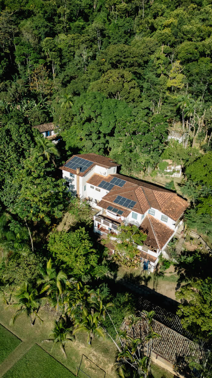 Vista aérea da casa-sede da fazenda, com telhado de placas solares, cercada pela floresta