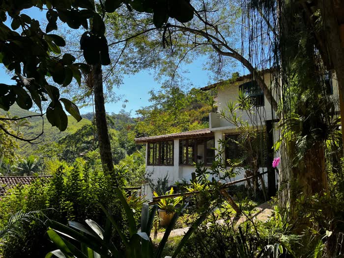 A casa-sede vista por entre o jardim tropical, sob o céu azul