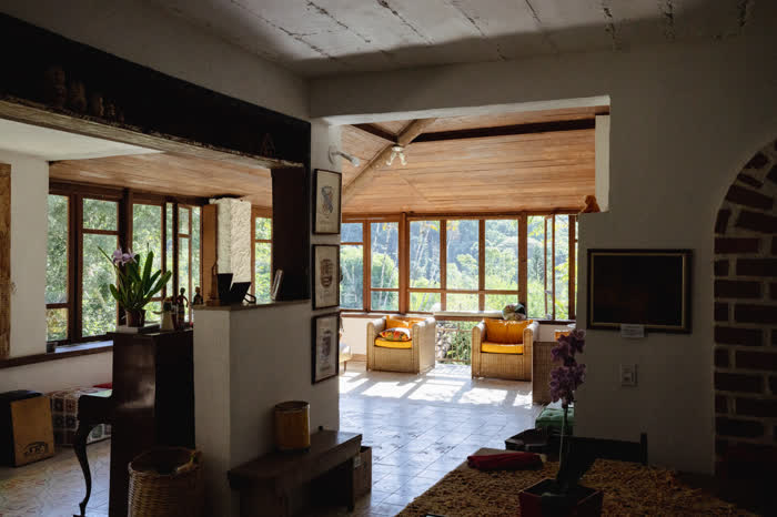 Sala da casa-sede com poltronas de vime, orquídeas e vista para a Mata Atlântica