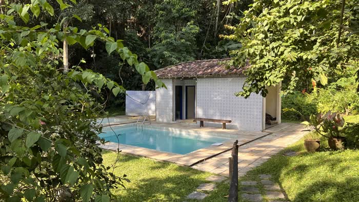 Piscina ao lado do vestiário de azulejos, cercada pela vegetação da fazenda