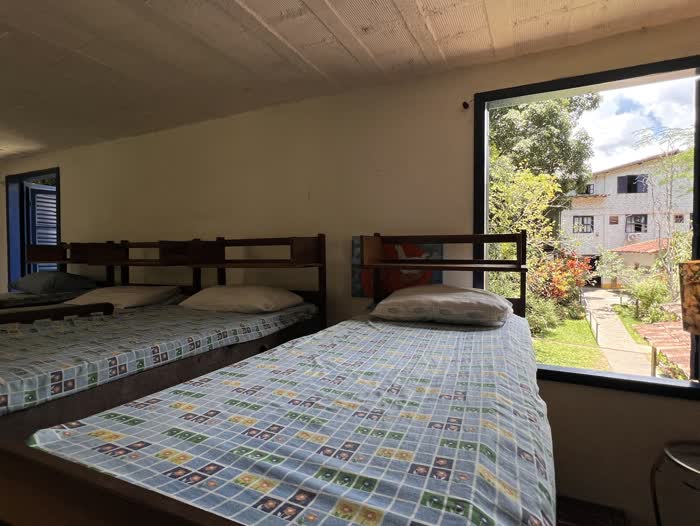 Quarto de beliches com o janelão aberto para o jardim e para o casarão de janelas azuis do outro lado do gramado