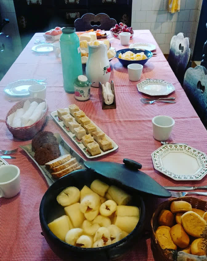 Mesa do café da roça da Fazenda dos Cordeiros: pães, bolos, compota de maçã e café passado sobre toalha xadrez
